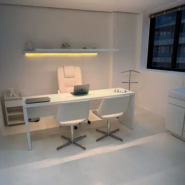 Consultório da Elvare, com mesa branca, poltronas e luz indireta